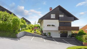 Uma casa de dois andares com uma escadaria de pedra que dá acesso à entrada, um espaço de estacionamento na frente e um jardim verdejante.