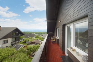 A balcony with a red-tiled floor, overlooking a residential area with houses and a mountain range in the distance. - Apartments Rikli Rodine near Bled (Žirovnica)