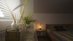 Quarto com um banco de madeira, uma mesa pequena com abajur e uma janela com persianas.