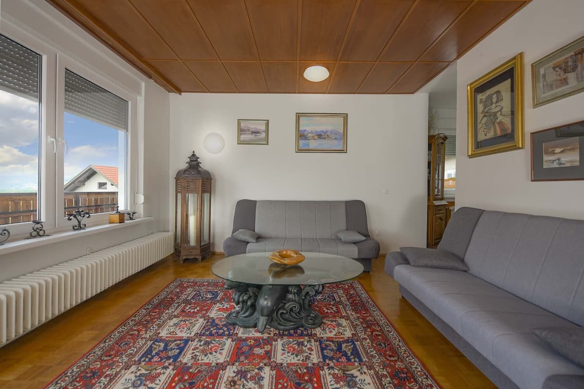 A living room with a grey sofa, a round glass coffee table, and a patterned rug.