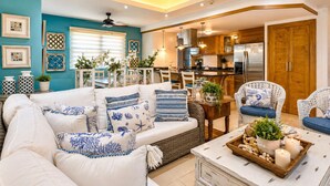 Een woonkamer met een bank, stoelen, een salontafel en een keuken met kasten en apparatuur.