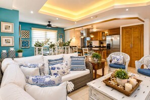Una sala de estar con sofá, sillas, una mesa de centro y una cocina con armarios y electrodomésticos.