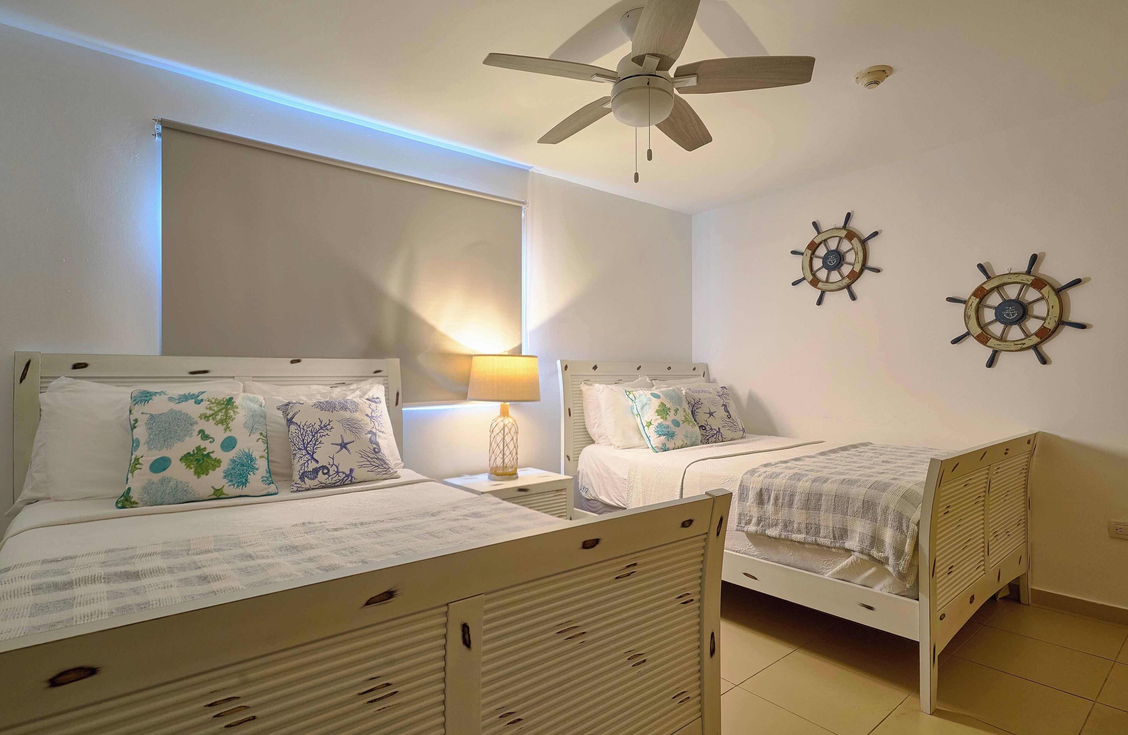A bedroom with two single beds, a ceiling fan, and wall-mounted ship's wheel decorations.