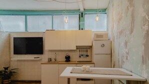 Une cuisine compacte avec des meubles blancs, un four à micro-ondes, un évier et une petite table sur laquelle se trouvent une théière et des tasses.