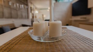 Une table sur laquelle sont posées trois bougies blanches, maintenues par un porte-bougie en verre transparent, le tout placé sur un set de table en fibres tressées, dans une pièce au décor intérieur moderne.