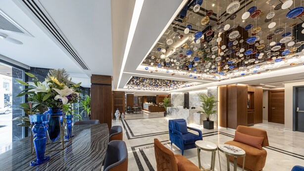 A modern lobby with a marble reception desk, blue and brown seating, and a ceiling adorned with hanging decorative plates. - Vital Hotel Fulya (Istanbul)