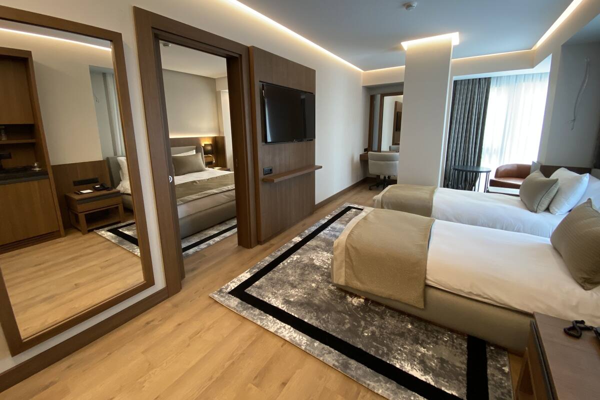 A modern hotel room with a large bed, a desk, a chair, a TV, and a bathroom visible through an open door.