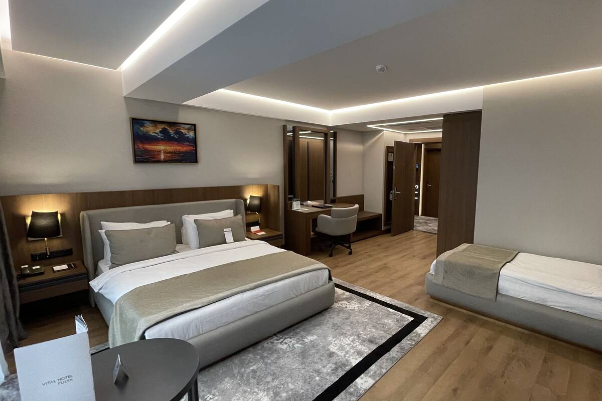 A modern hotel room with a large bed, a smaller bed, a desk, and a chair.