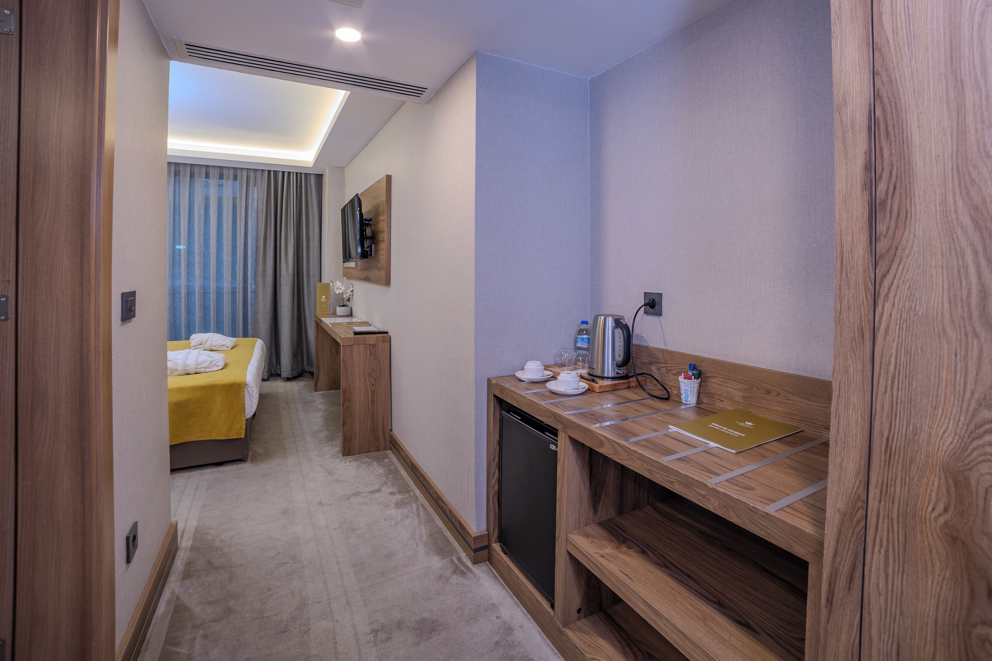 A hotel room with a bed, a desk with a coffee maker, and a small refrigerator.
