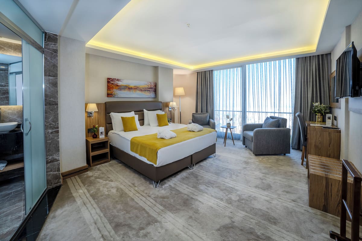 A modern hotel room with a large bed, a seating area, a TV, and a bathroom with a marble countertop.