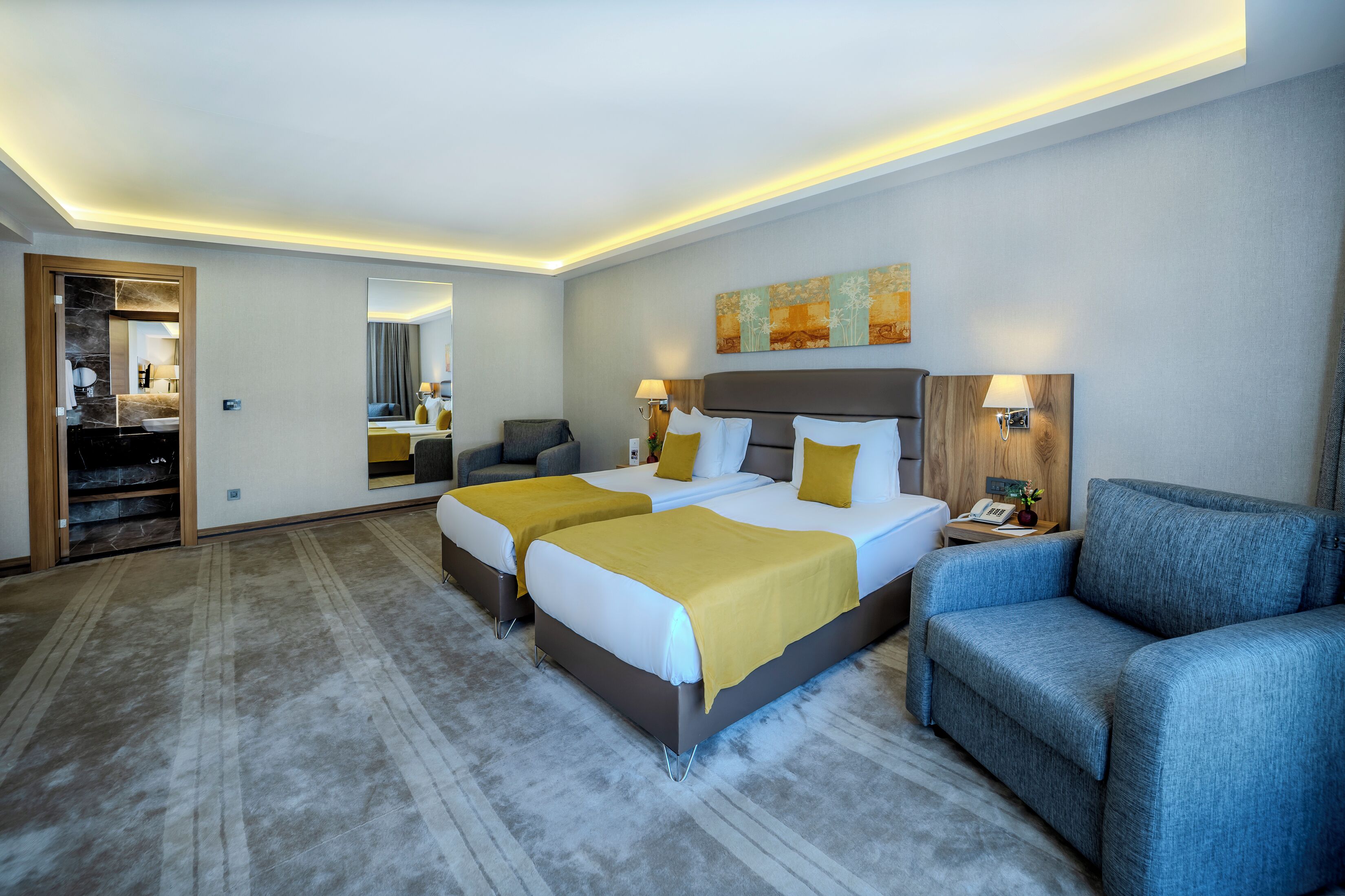 A hotel room with two beds, a sofa, a mirror, and a nightstand with a lamp.