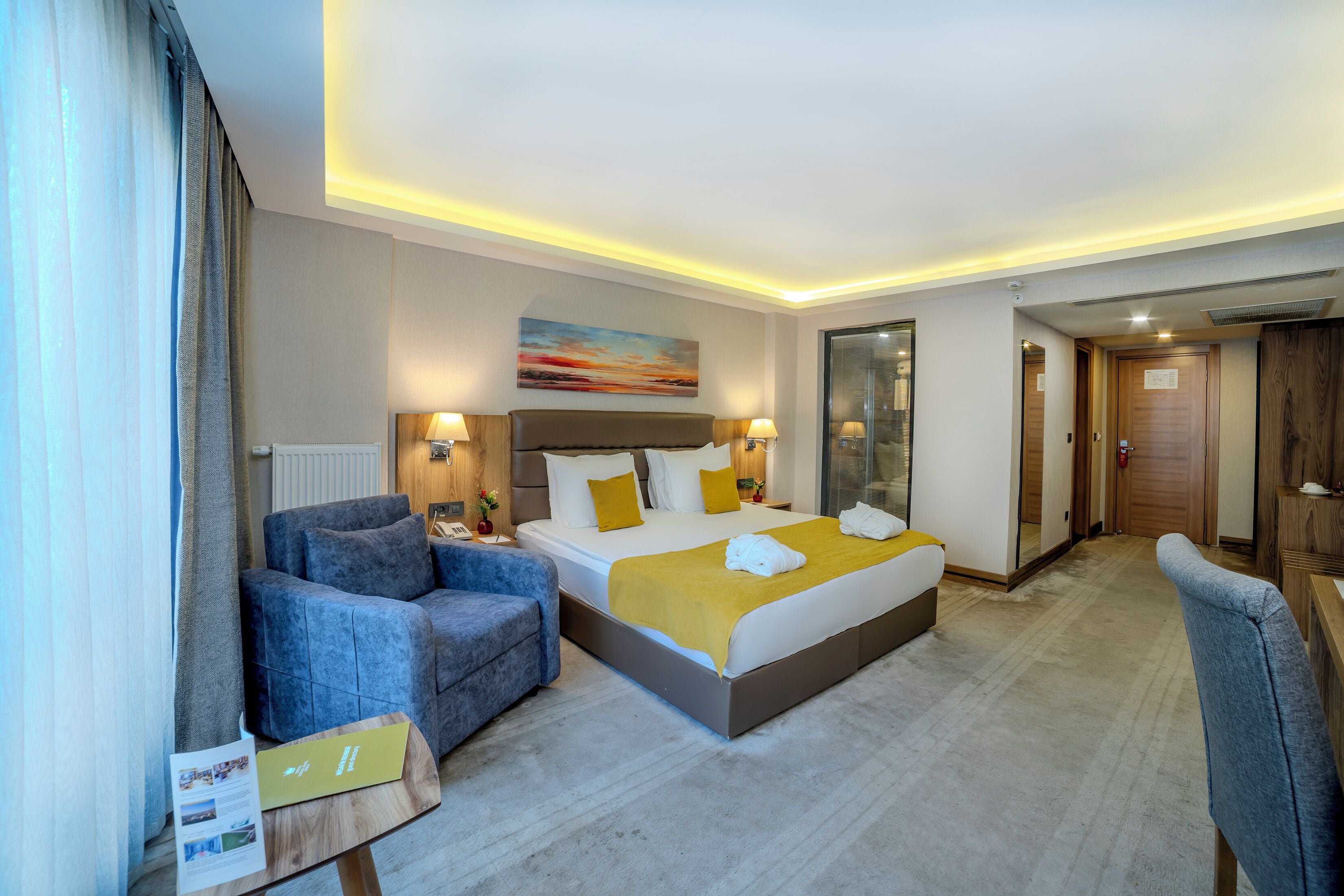 A hotel room with a bed, a sofa, a small table, and a mirror.