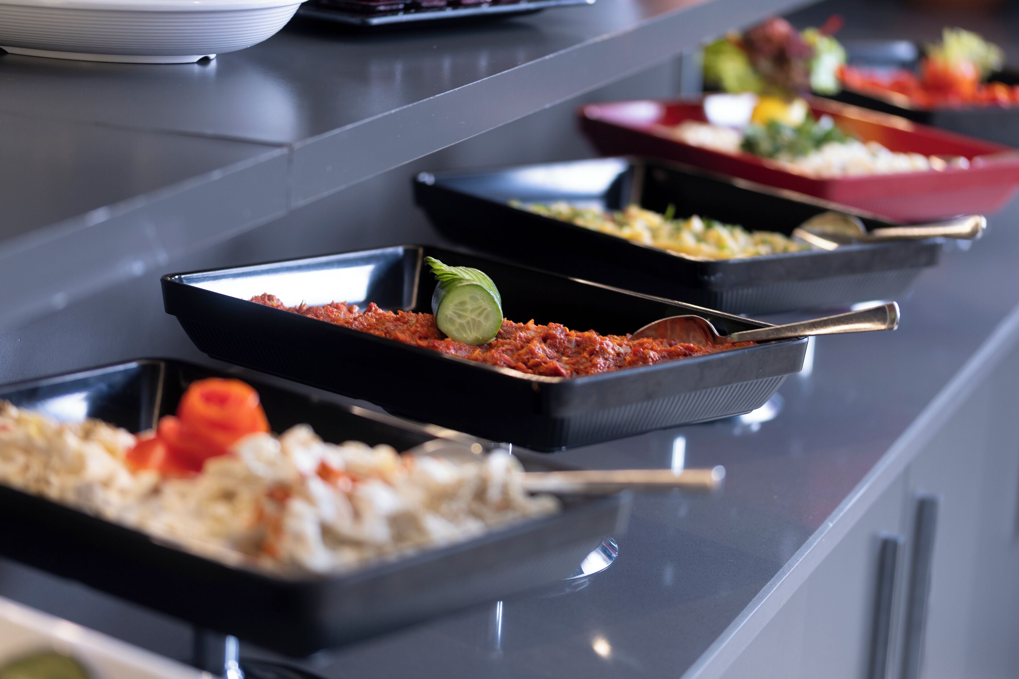 A buffet with various dishes in black trays, including pasta and rice.