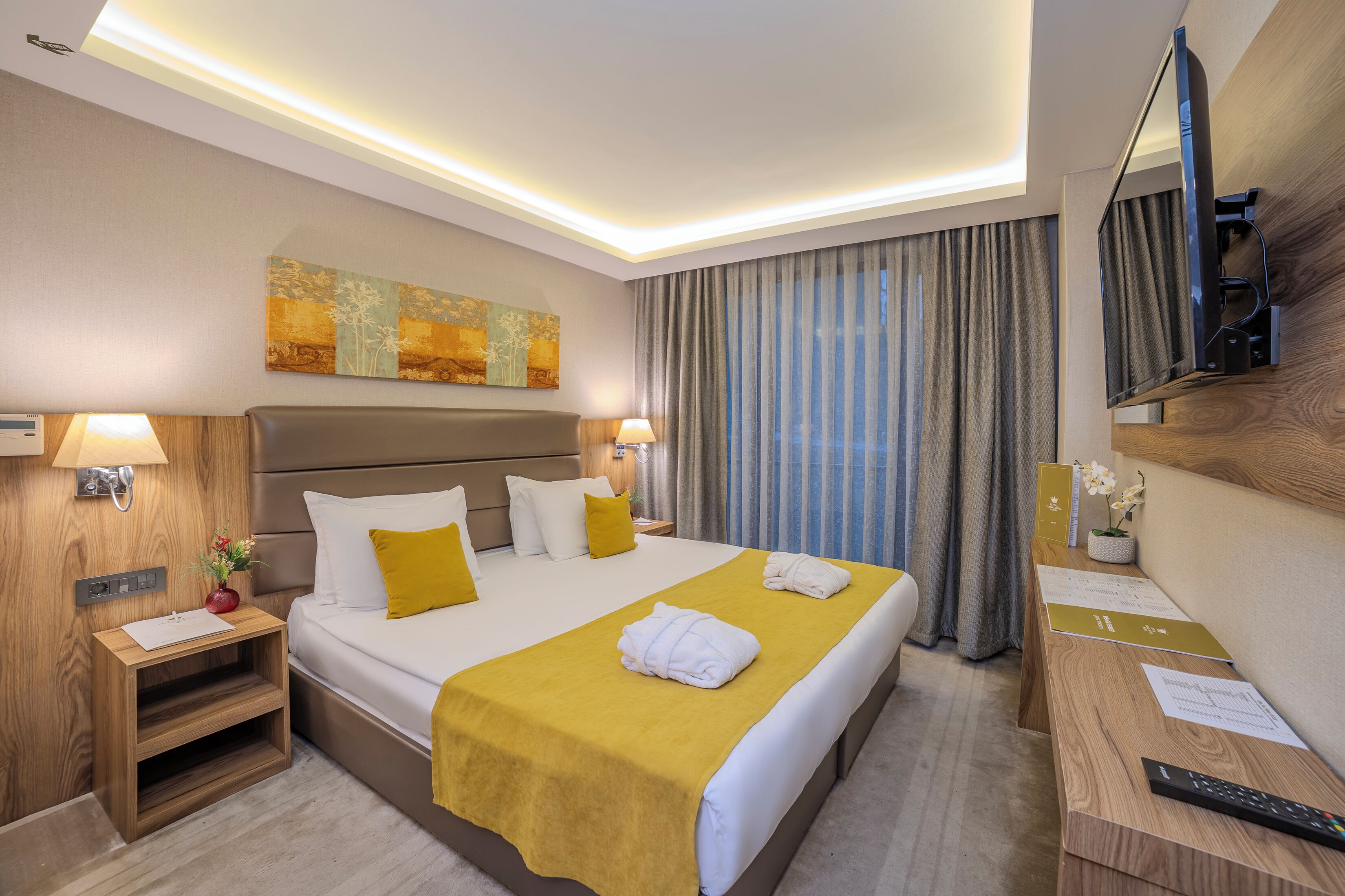A hotel room with a large bed, bedside lamps, a desk with a remote control, and a television mounted on the wall.