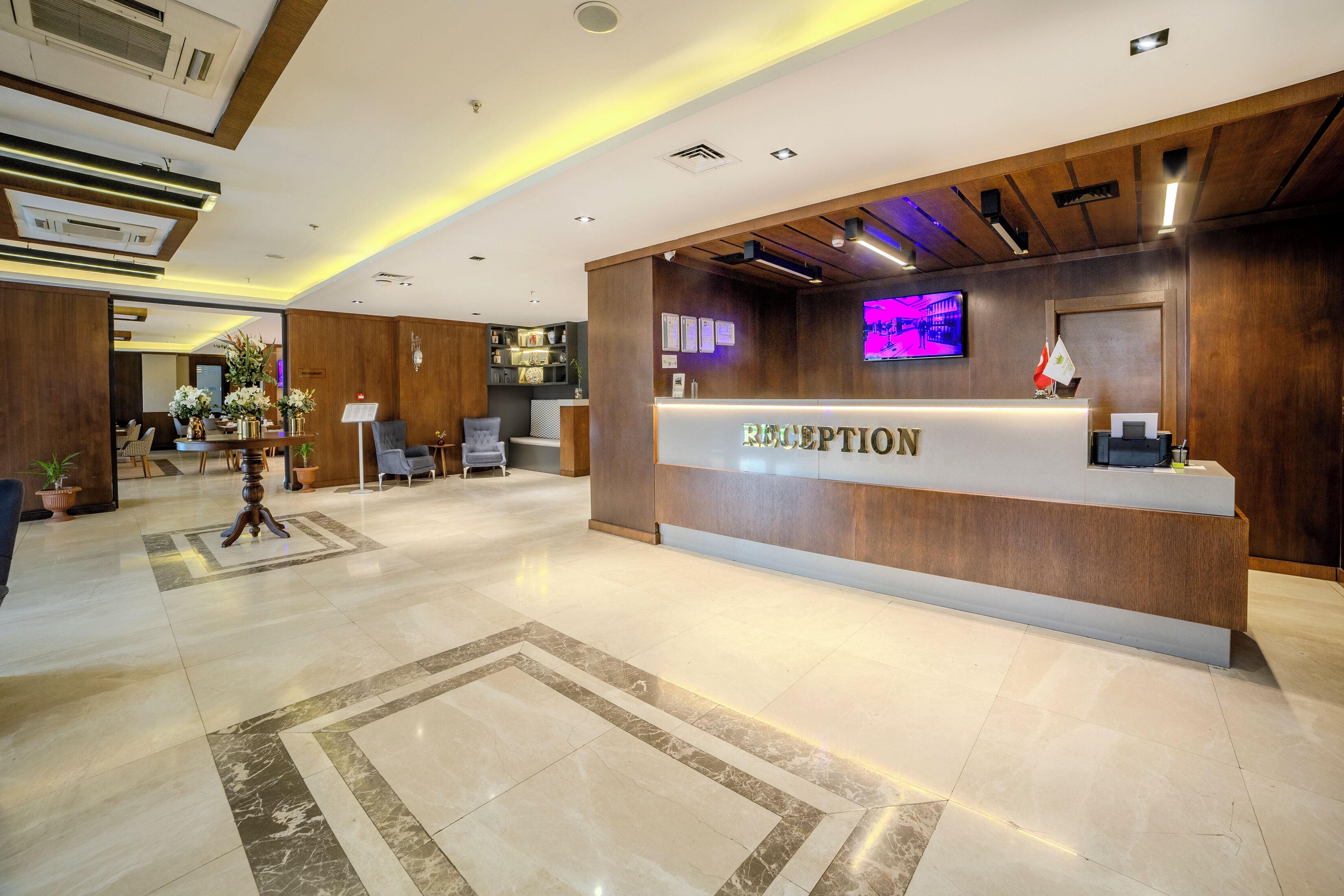A reception area with a wooden reception desk, a flat-screen TV, and a potted plant.