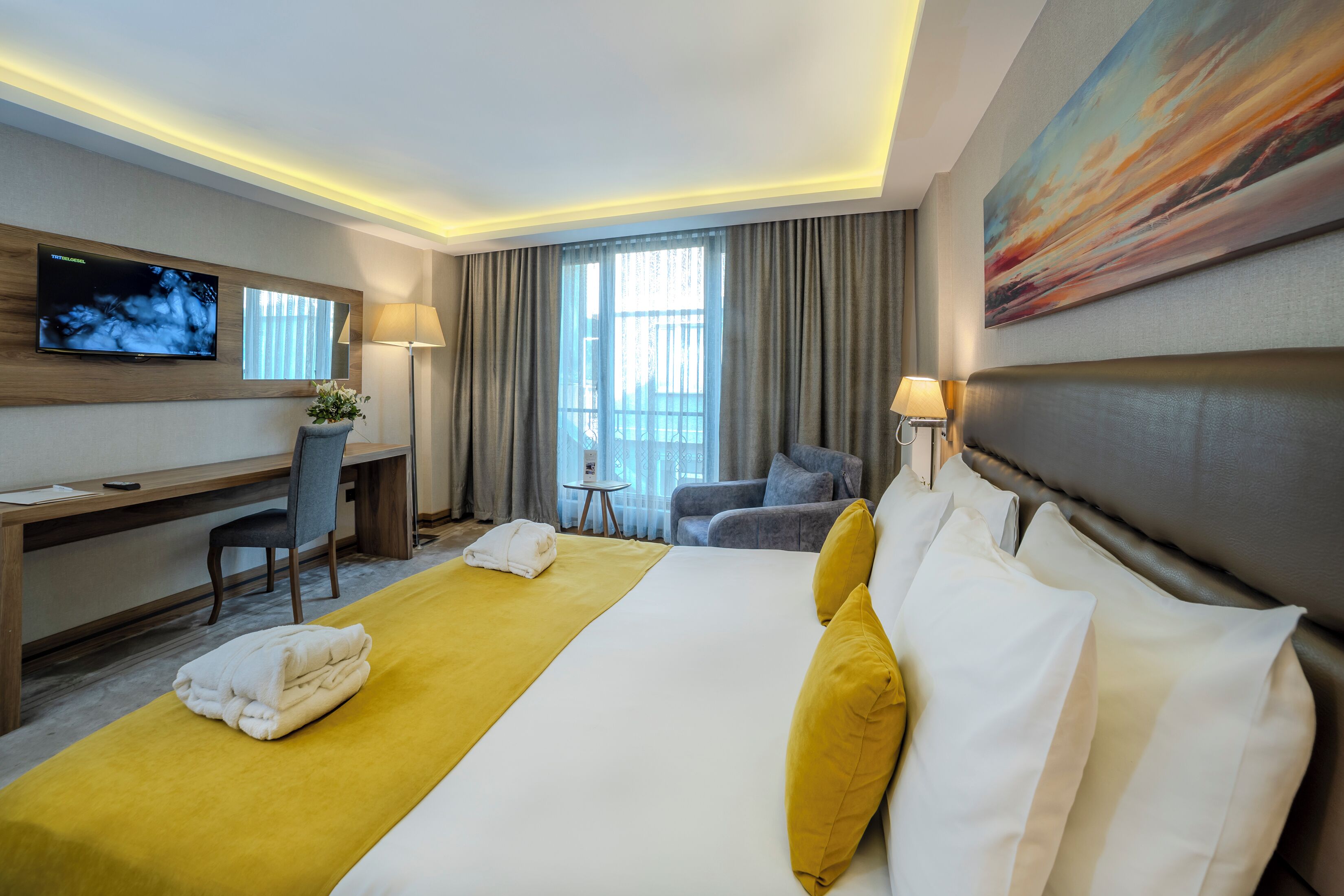 A hotel room with a large bed, a desk, a TV, and a painting on the wall.