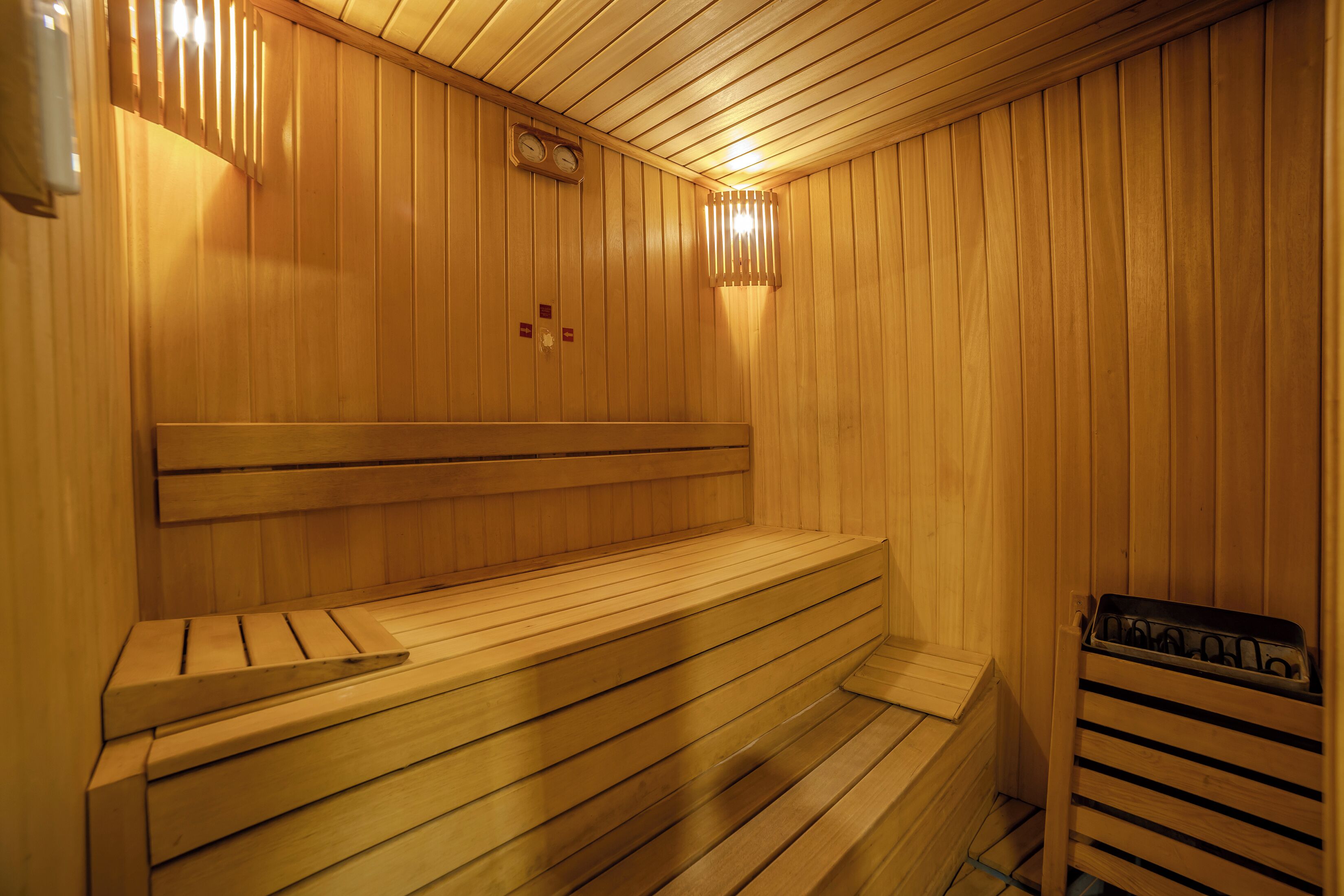 A wooden sauna with benches and a bench seat, a wall-mounted heater, and a ventilation system.