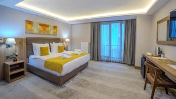 A modern hotel room with a large bed, bedside tables, a desk, and a large window with curtains.