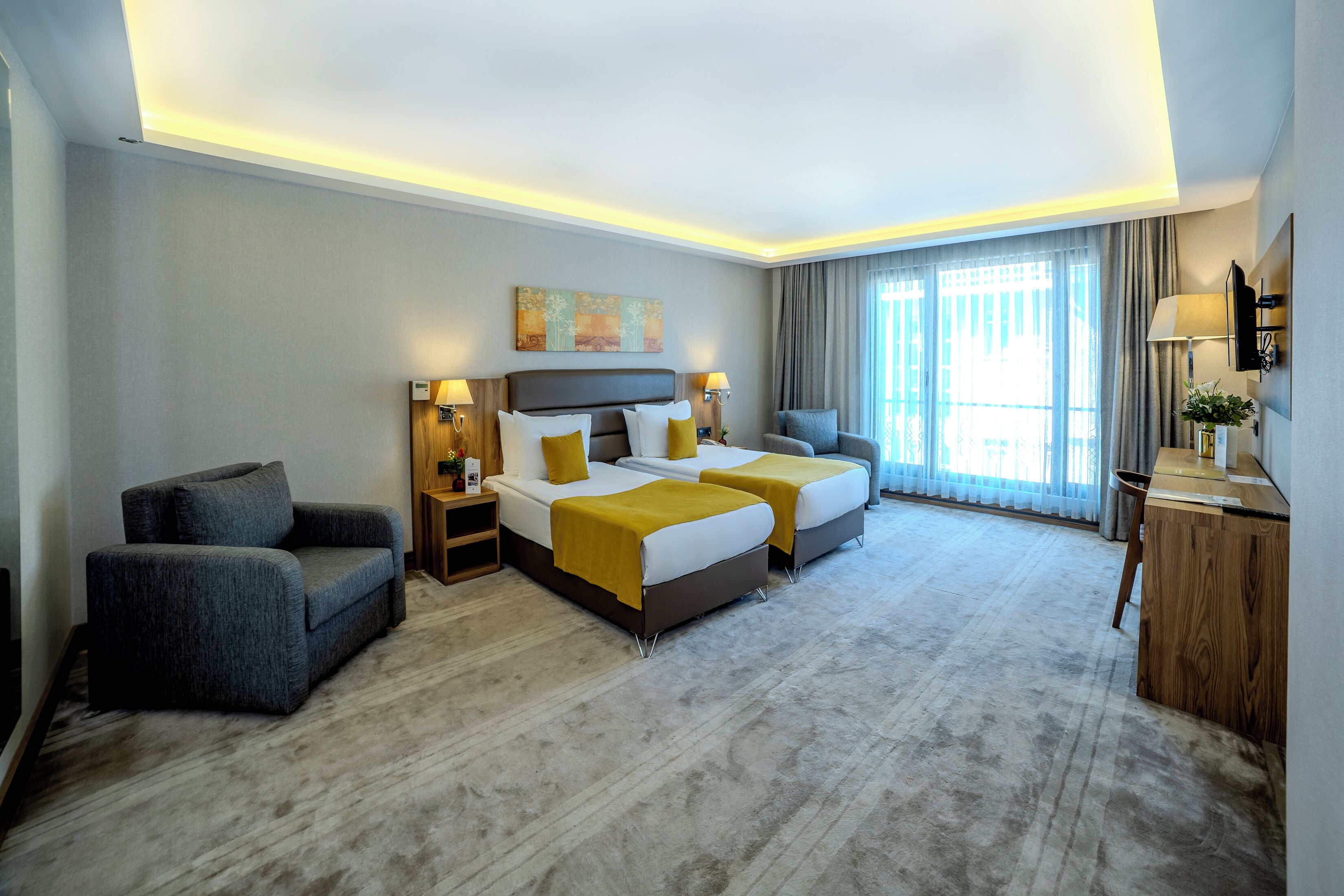 A hotel room with two beds, a sofa, a desk, and a large window with curtains.