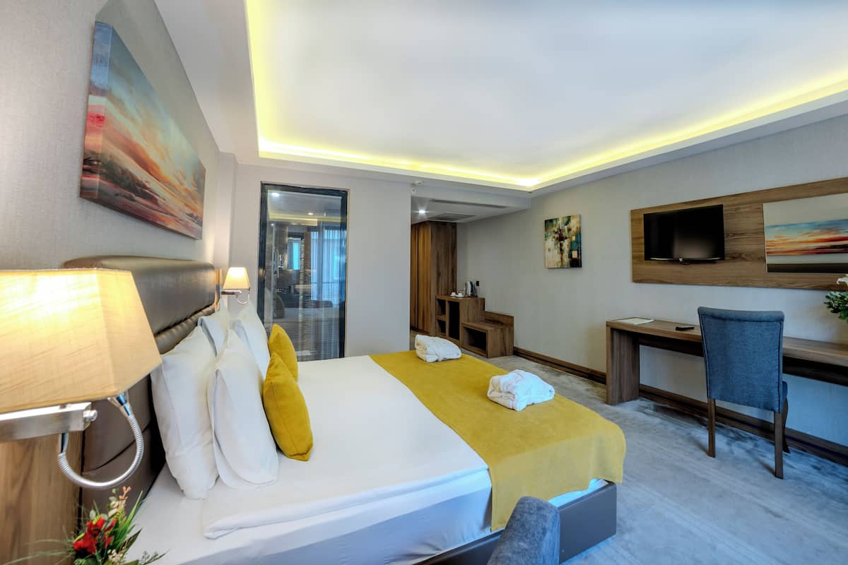 A hotel room with a bed, desk, chair, TV, and artwork.