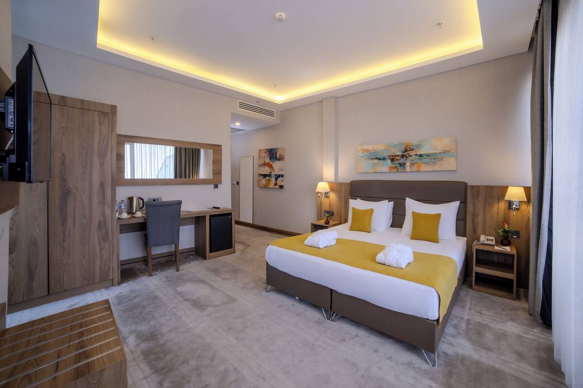 A hotel room with a large bed, a desk, a chair, a TV, and artwork on the walls.