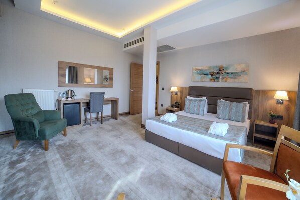 Una habitación de hotel con una cama grande, un escritorio, una silla y un sillón verde.