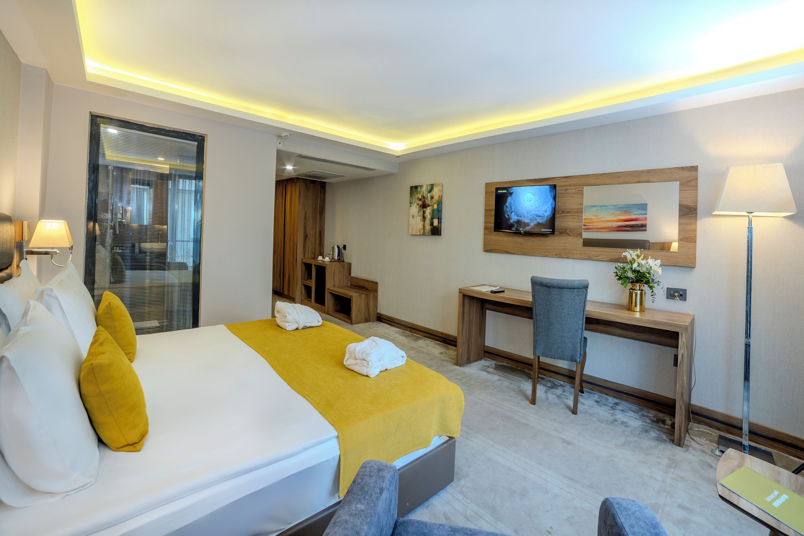 A hotel room with a bed, a desk, a chair, a TV, and a lamp.