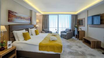 A hotel room with a large bed, a sofa, a TV, and a window with curtains.