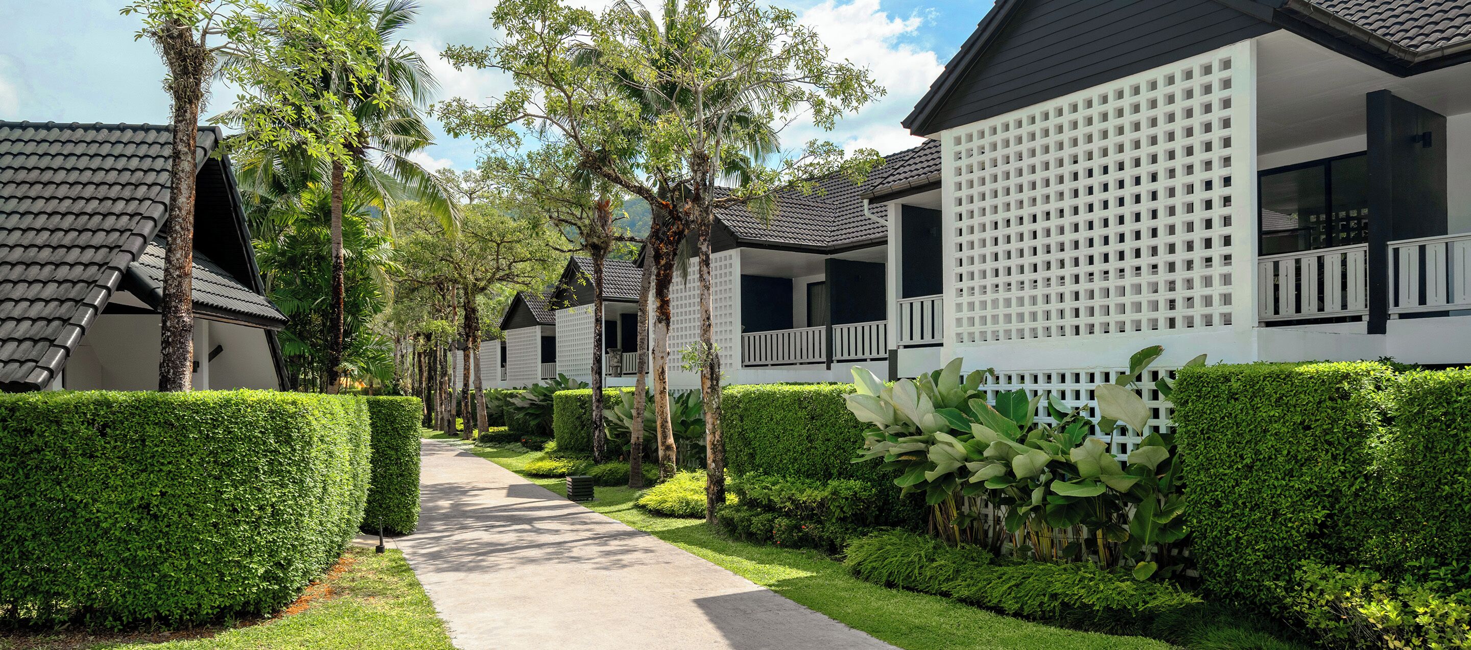 Una hilera de villas modernas con un camino bordeado por setos cuidados y palmeras.