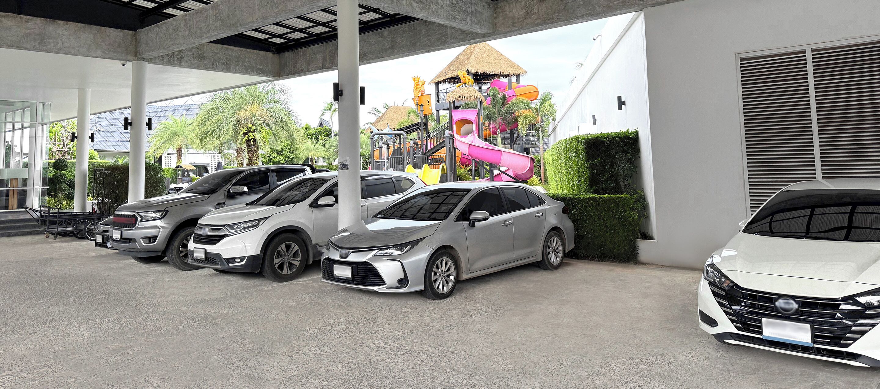 A parking area with several cars, a covered walkway, and a colorful play structure in the background.