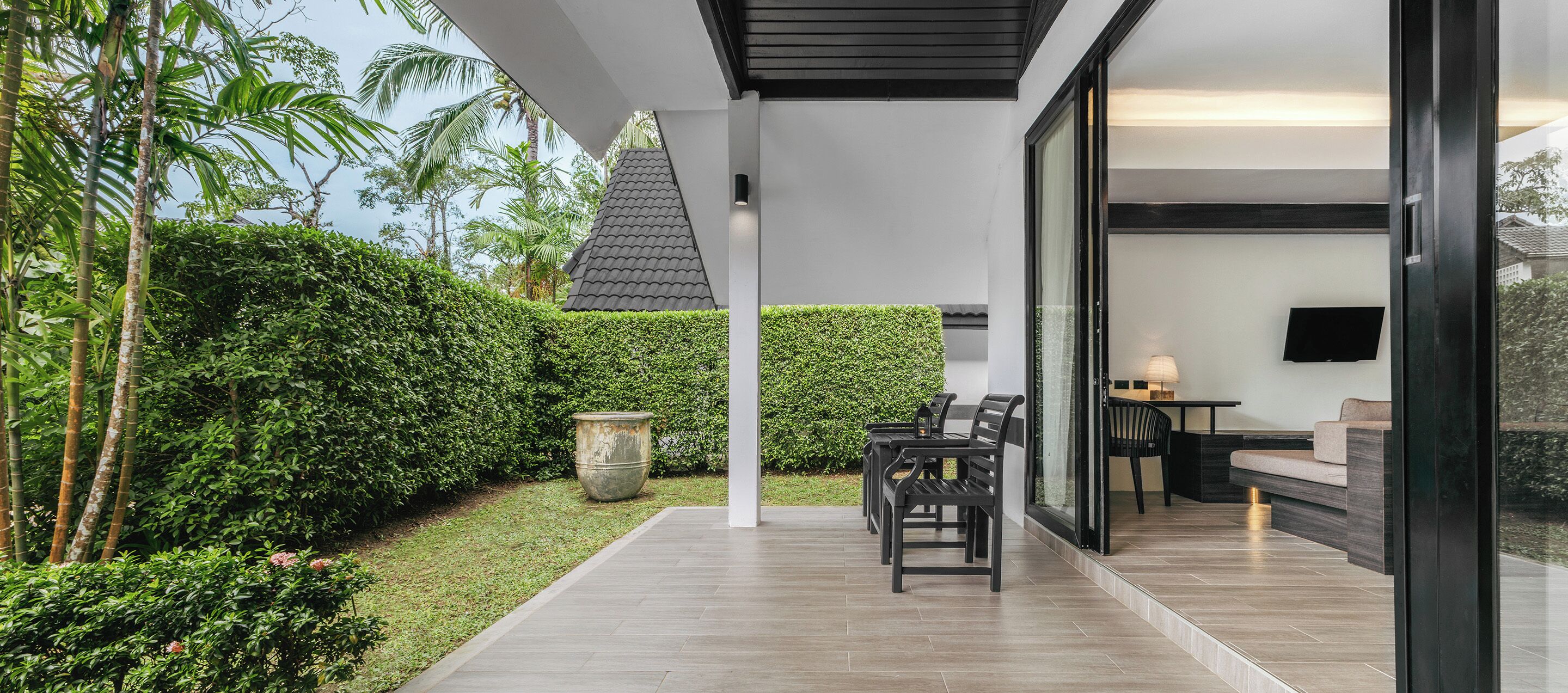 A modern outdoor patio with a seating area, a large planter, and a view of the surrounding greenery.