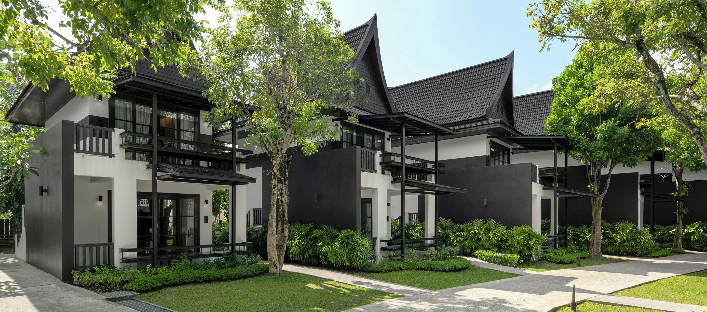 A modern building with a black and white facade, multiple balconies, and a well-maintained garden.