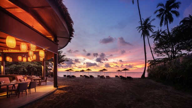 A beachside restaurant with outdoor seating and umbrellas, overlooking the ocean at sunset. - The Splash Koh Chang (Ko Chang)