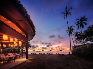 A beachside restaurant with outdoor seating and umbrellas, overlooking the ocean at sunset. - The Splash Koh Chang (Ko Chang)