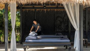 A bed with a canopy, a person adjusting the bed, and a thatched roof structure.