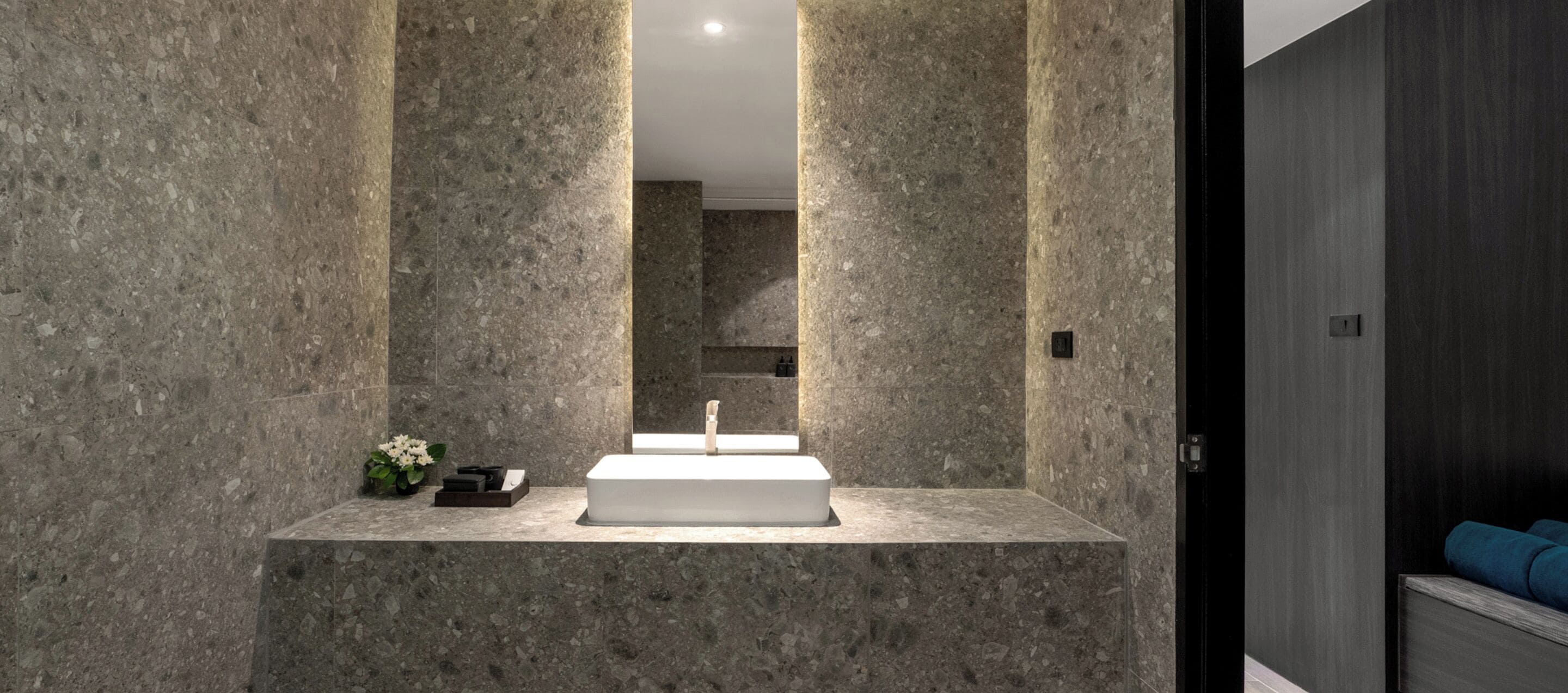 A bathroom with a rectangular sink, marble walls, and a dark wooden door.