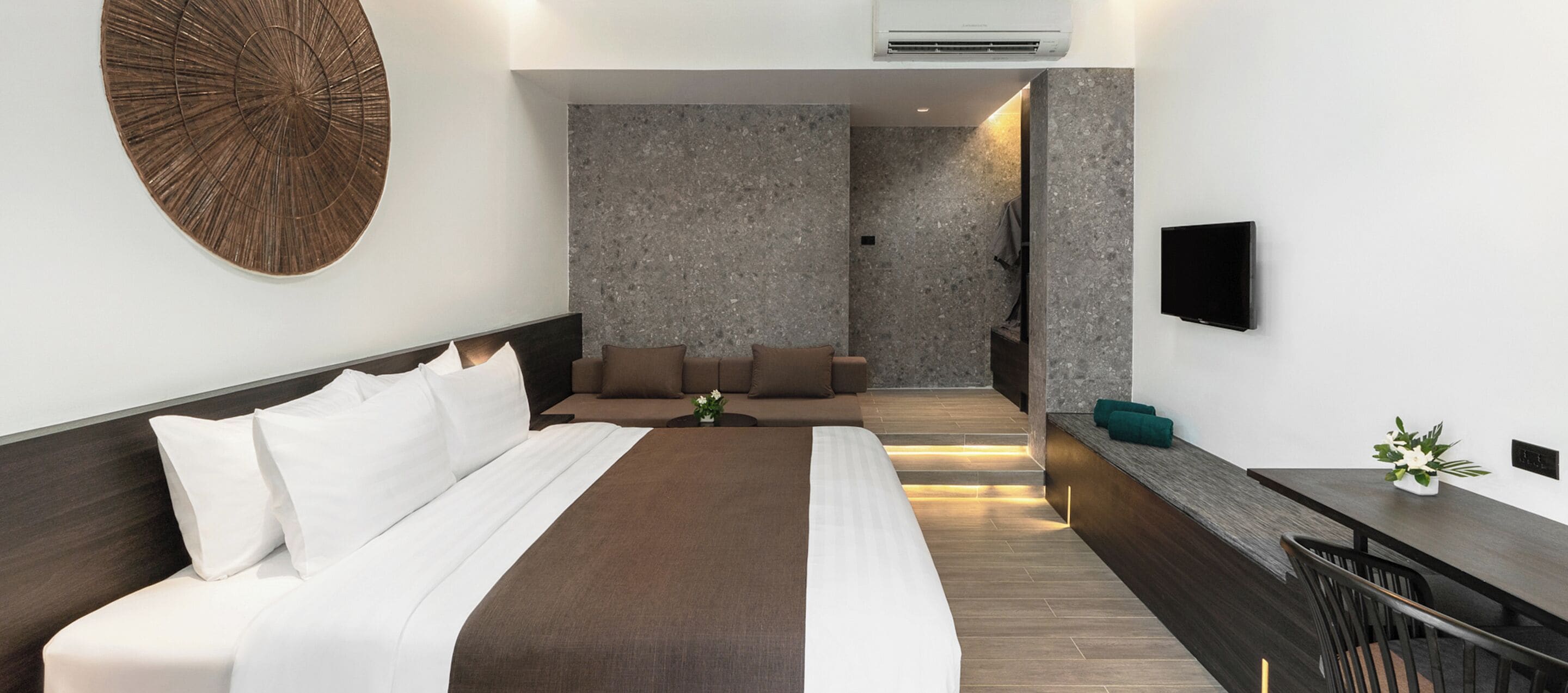Una habitación de hotel moderna con una cama grande, una zona de estar, un televisor de pantalla plana y una mesita con un jarrón de flores.