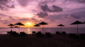 A beach with lounge chairs and umbrellas under a sunset sky. - The Splash Koh Chang (Ko Chang)