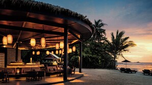 A beachside restaurant with outdoor seating, a bar area, and a view of the ocean at sunset. - The Splash Koh Chang (Ko Chang)