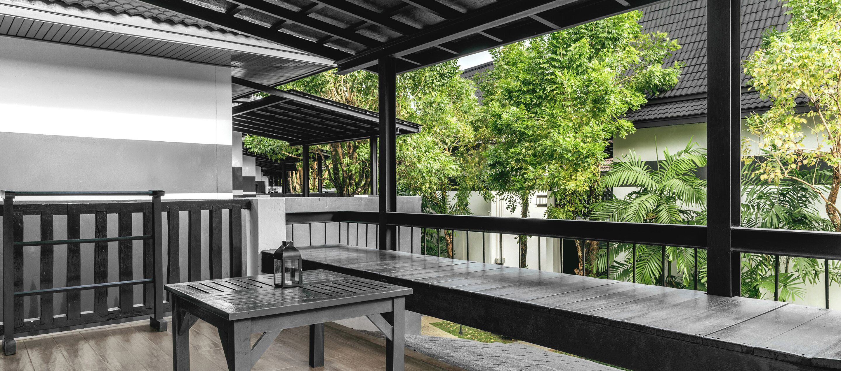 A balcony with a table and chairs, a lantern, and a view of greenery and buildings.