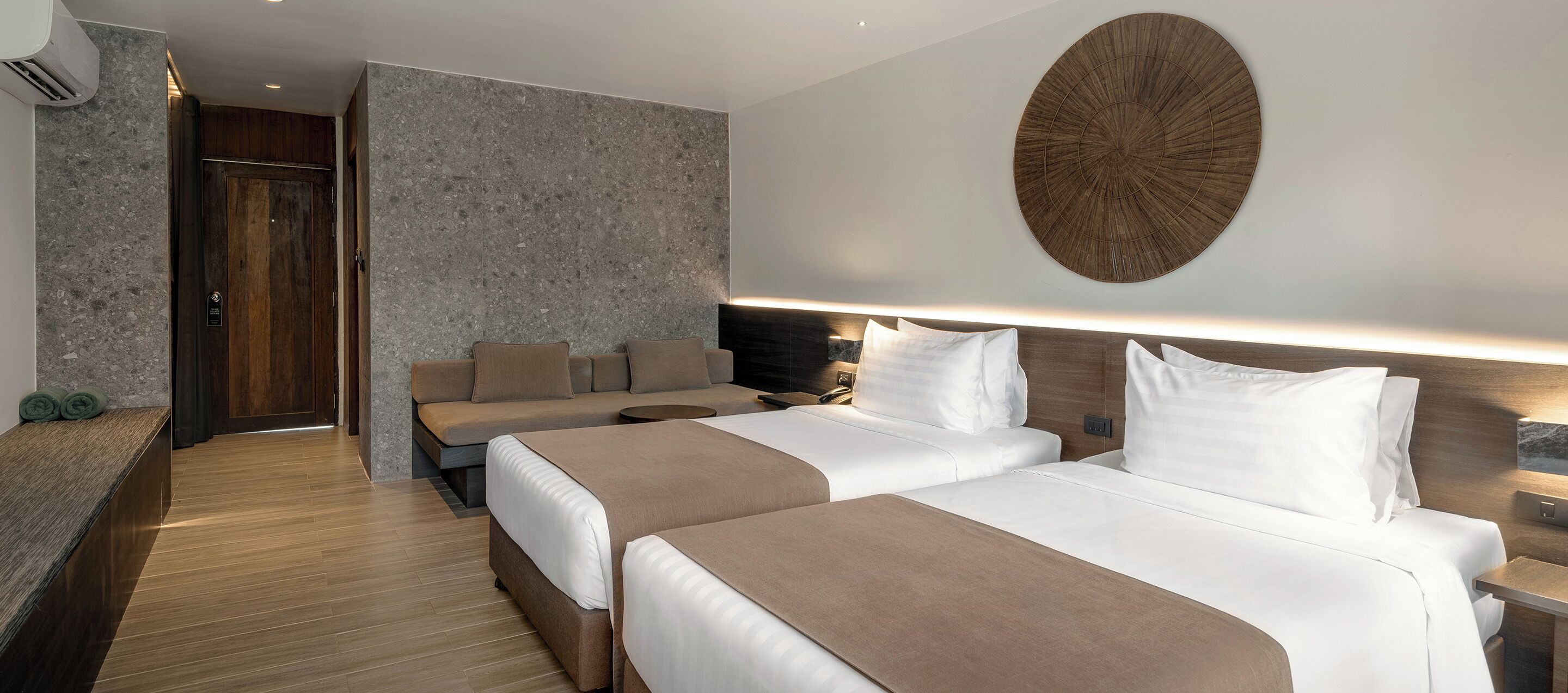 A hotel room with two beds, a sofa, a round wall decoration, and a wooden headboard.