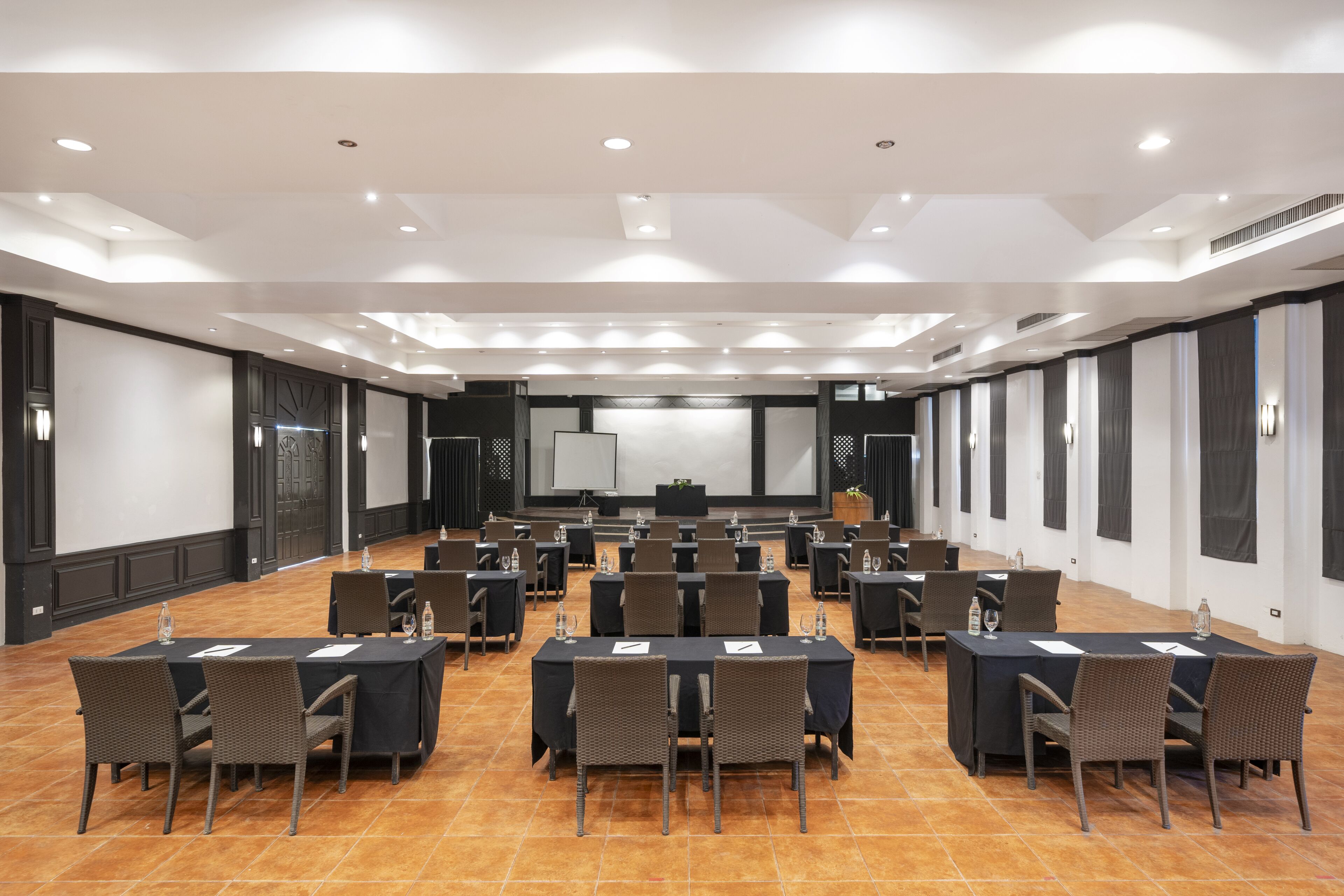 Sala de conferências com várias mesas e cadeiras, equipada com garrafas de água e documentos.