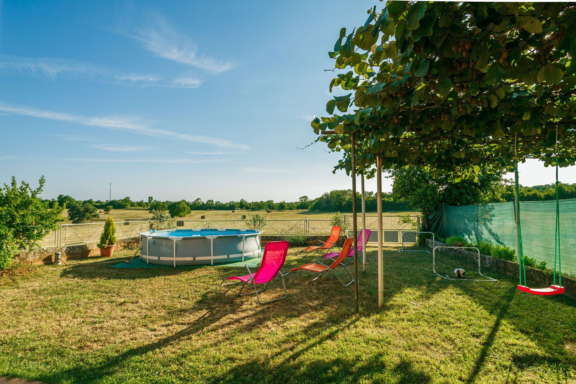 A backyard with a swimming pool, lounge chairs, and a swing set.