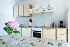 A kitchen with a gas stove, oven, and coffee maker. There is a vase with a pink flower on the table.