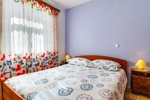 A bedroom with a bed, two bedside lamps, a nightstand, and a window with curtains.