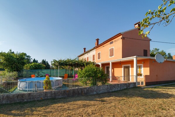 A two-story house with a swimming pool, a satellite dish, and a garden.