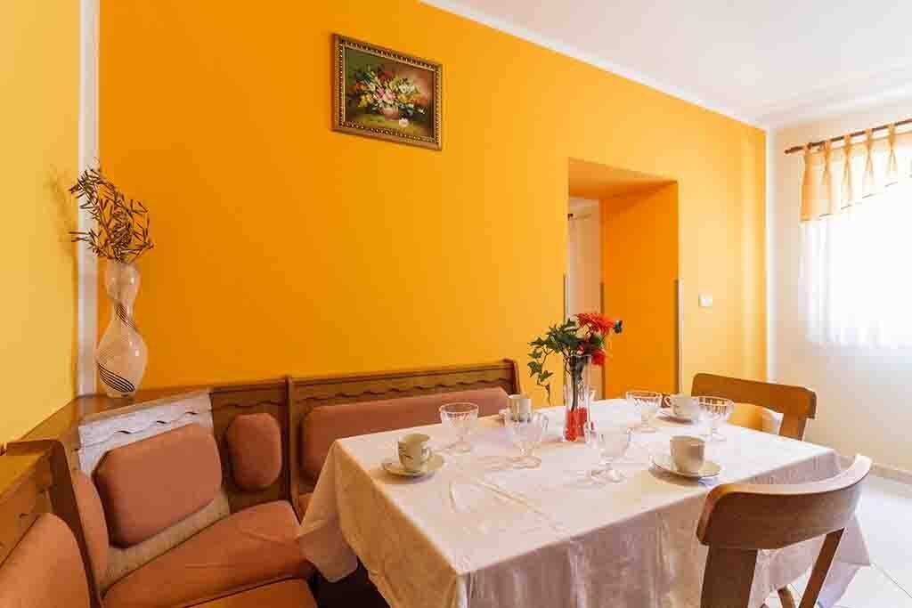 A dining area with a table set for four, a vase of flowers, and a painting on the wall.