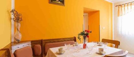 A dining area with a table set for four, a vase of flowers, and a painting on the wall.