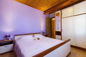 Ein Schlafzimmer mit Holzbalkendecke, einem Bett mit weißer Bettdecke, zwei Nachttischen mit Lampen und einem Kleiderschrank.