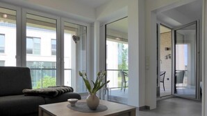 Un salon moderne avec un canapé, une petite table sur laquelle est posé un vase, et de grandes fenêtres donnant sur l’extérieur.
